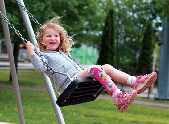 A young female leg amputee plays on the swings at a playground.