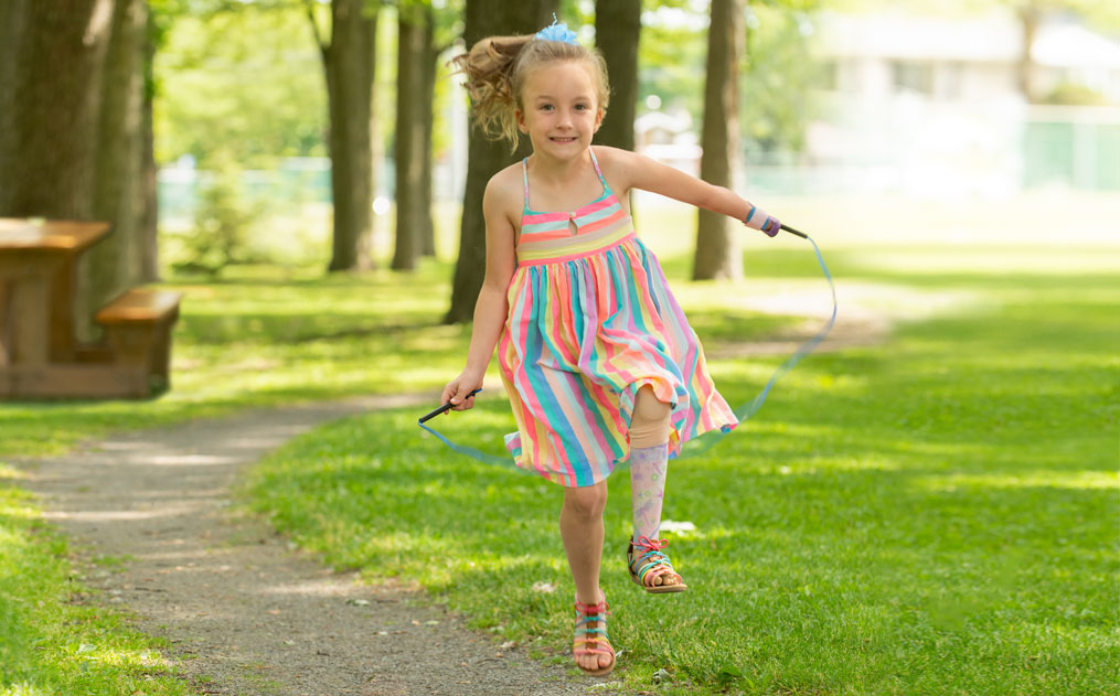 Une fillette portant une jambe artificielle joue à la corde à sauter dans un parc.