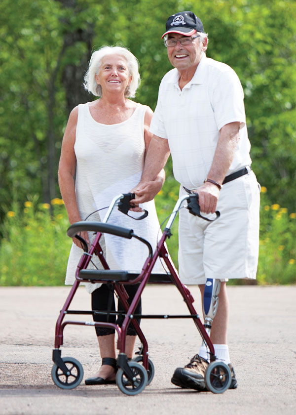 Un homme âgé amputé d’une jambe se tient debout à côté de sa conjointe, à l’extérieur.