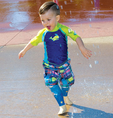 Un jeune garçon amputé des deux jambes joue dans une aire de jeux d’eau.