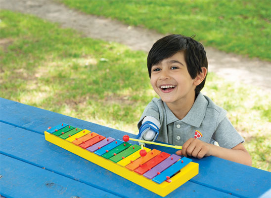 Un jeune garçon amputé d’un bras est assis à une table à pique-nique et joue du xylophone.