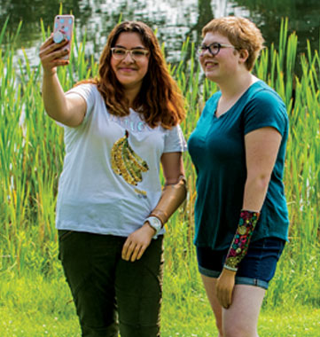 Deux adolescentes, l’une amputée d’un bras et l’autre d’une main, sont debout devant un étang et prennent un égoportrait.