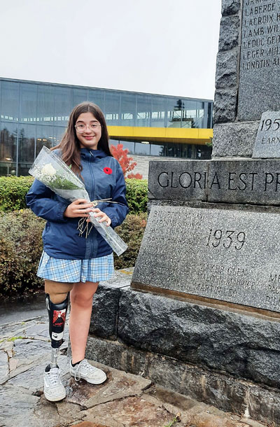 Une jeune adolescente amputée d’une jambe est debout à côté d’un cénotaphe et tient une rose blanche.