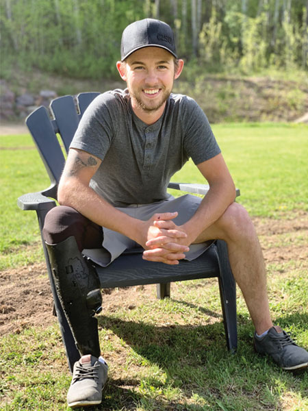 Un jeune homme amputé d’une jambe, portant sa prothèse, est assis à l’extérieur sur une chaise Muskoka.