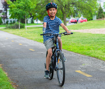 Un jeune garçon amputé d’un bras fait du vélo sur une piste cyclable dans un parc.