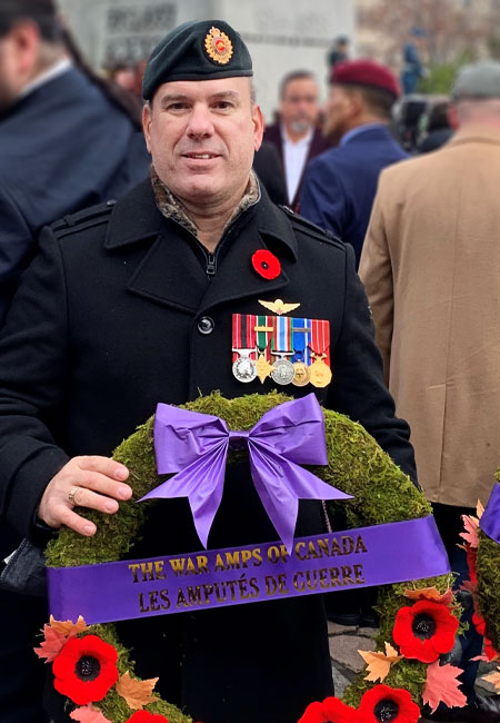 Un vétéran amputé de l’ère moderne tient une couronne au nom de l’Association des Amputés de guerre devant le Monument commémoratif de guerre du Canada.