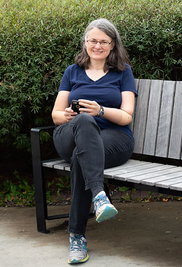 Une femme amputée d’un bras assise sur un banc de parc se sert de son téléphone cellulaire.
