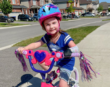Une jeune fille amputée d’un bras fait du vélo sur le trottoir.