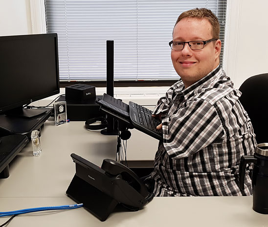 Un homme amputé des deux bras utilise un clavier d’ordinateur adapté en étant assis à son bureau de travail.