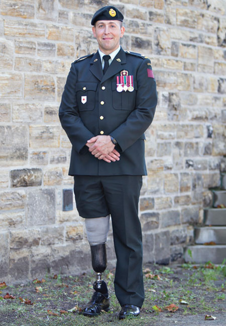 Un vétéran de l’ère moderne amputé d’une jambe porte son uniforme et se tient à côté d’un mur de pierre.
