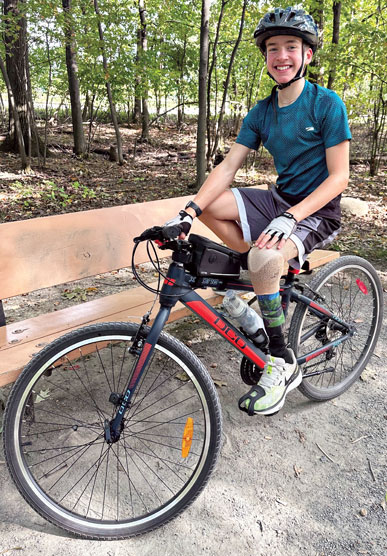 Un adolescent amputé d'une jambe fait du vélo sur un sentier forestier.