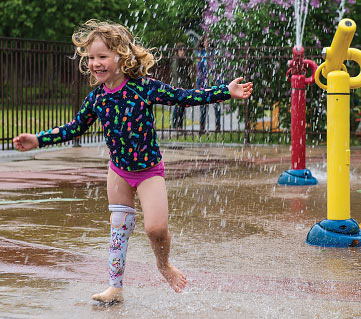 Jeanne, une enfant amputée, s’amuse dans les jeux d’eau à l’aide de sa jambe artificielle à l’épreuve de l’eau.