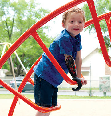 Nathan, amputé d’une partie du bras droit, s’amuse dans les jeux au parc à l’aide d’un appareil conçu à cet effet.