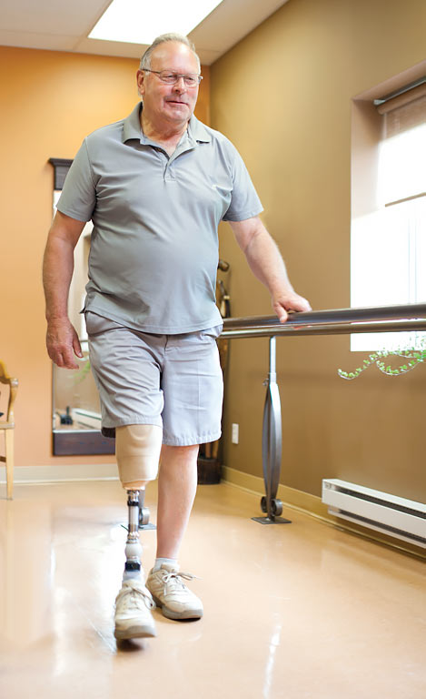 Un homme amputé marche à l’aide de sa prothèse en tenant la barre d’appui. 