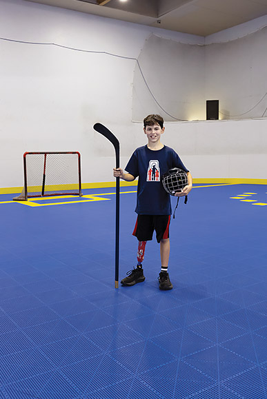 Hugo, debout dans un gymnase, porte sa jambe artificielle et tient un casque et un bâton de hockey.
