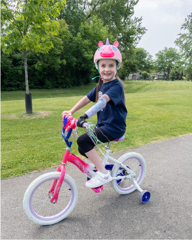 Kenzie, a young girl wearing an artificial arm riding her bicycle.