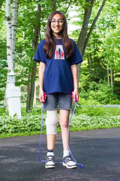 Madison, a young girl wearing an artificial leg standing on the pavement with a jump rope.