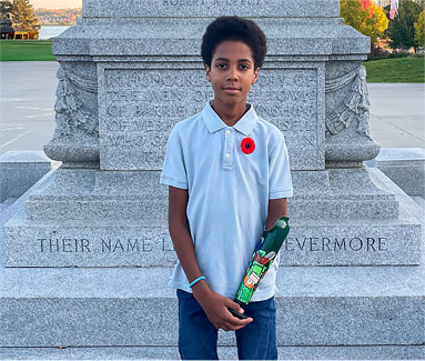 Deji, un jeune garçon amputé d’un bras, est debout devant un monument commémoratif.