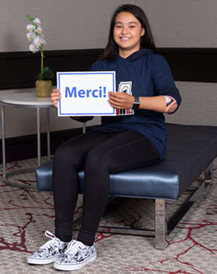 Une jeune fille amputée portant un bras artificiel tient un écriteau sur lequel il est inscrit « Merci! ».